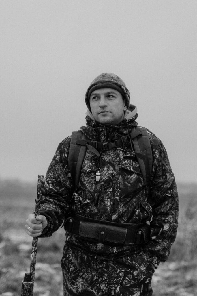 Monochrome portrait of a hunter in camouflage with a rifle outdoors, showcasing military gear.