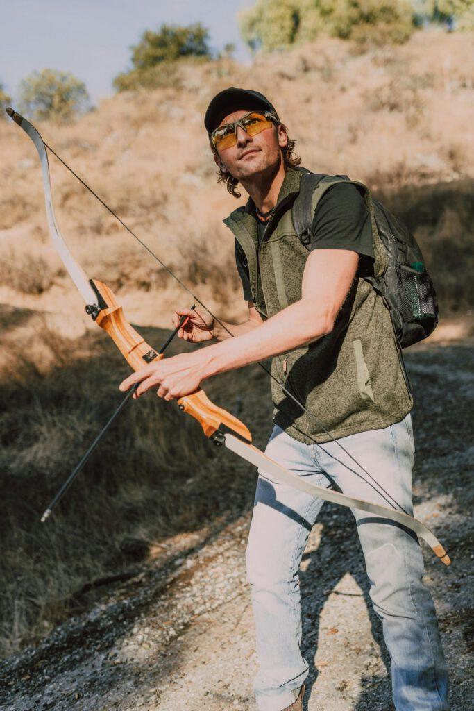 A man holding a bow and arrow, enjoying archery practice outdoors on a sunny day.